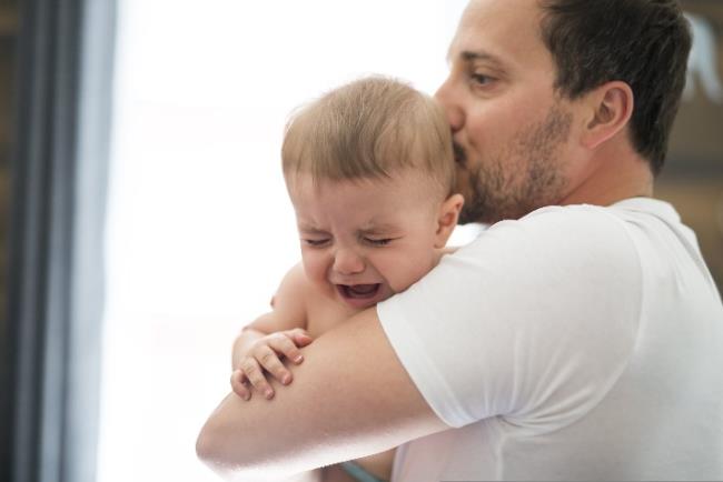 גבר מחזיק תינוק קטן שבוכה ומנסה להרגיע אותו